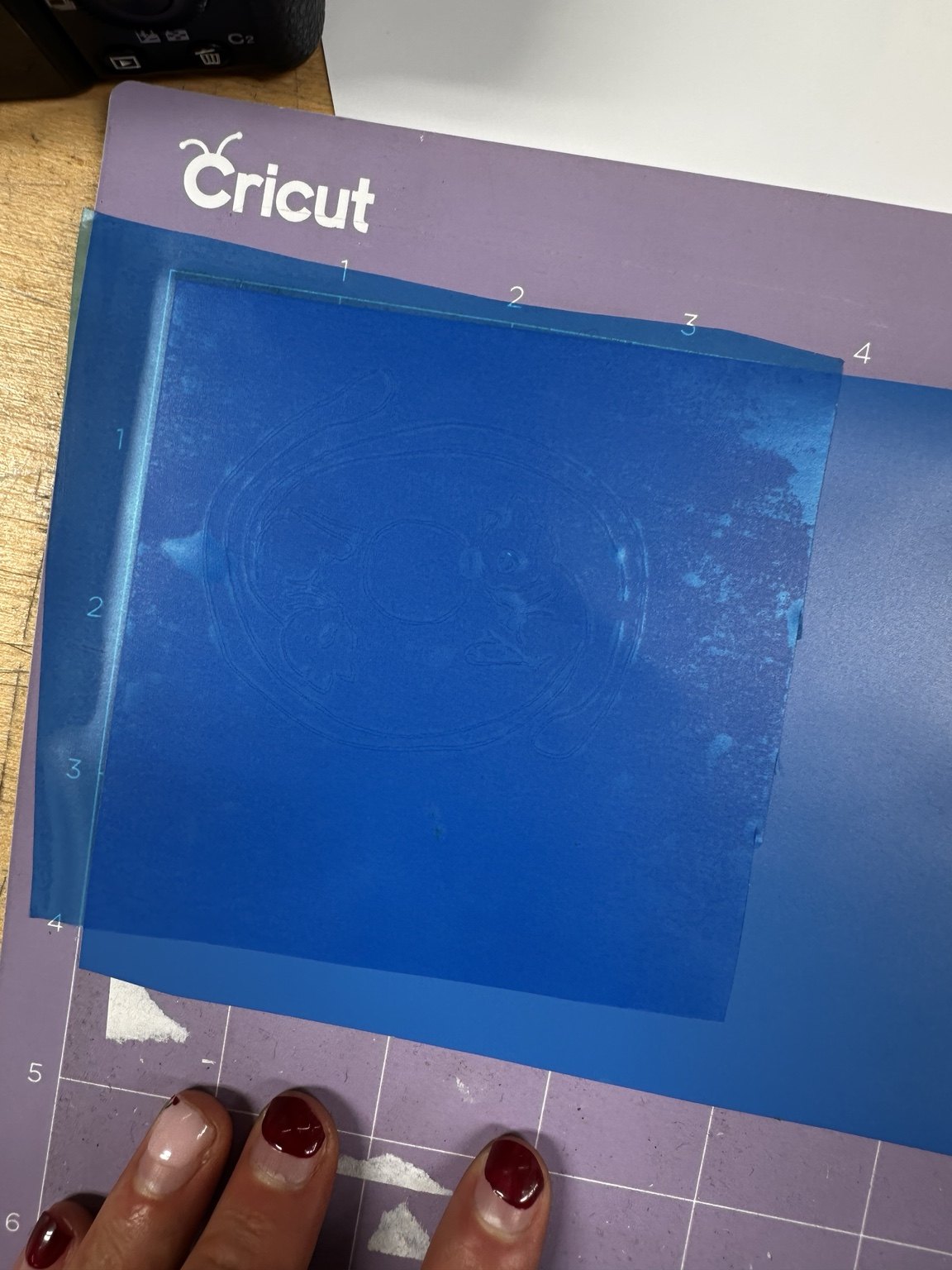 Blue vinyl sheet on a Cricut cutting mat with the design outline faintly visible