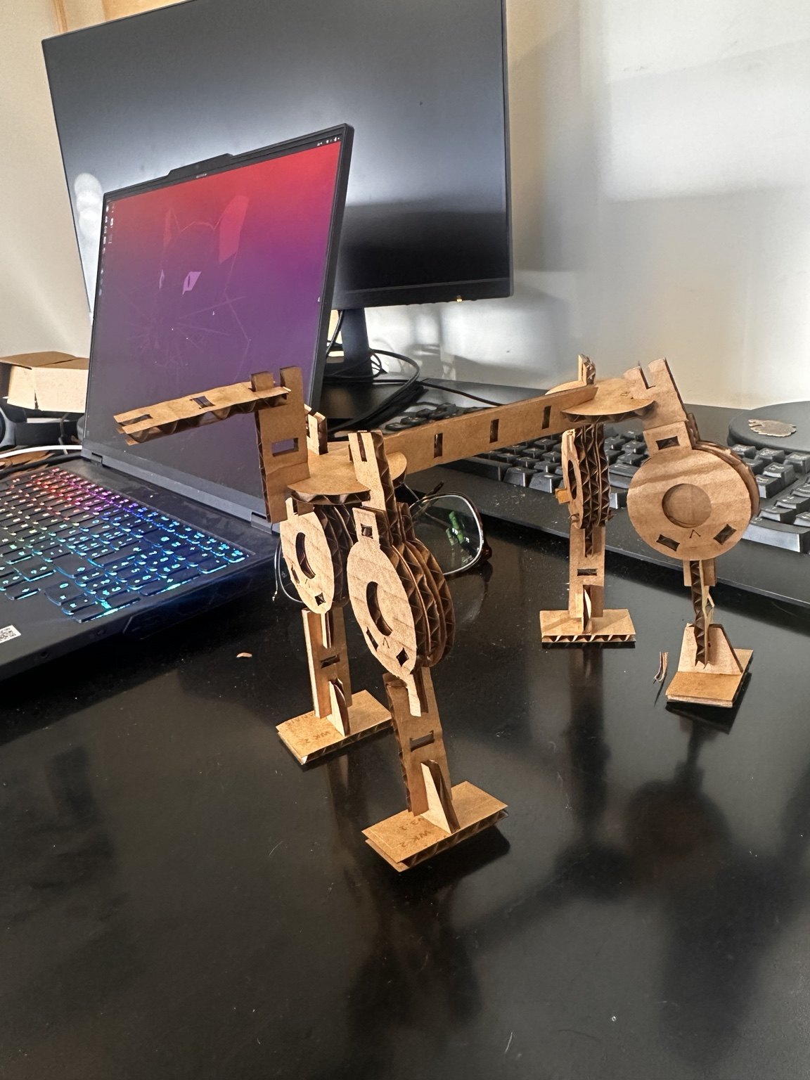 Finished brown laser-cut cardboard quadruped, photographed beside a laptop
