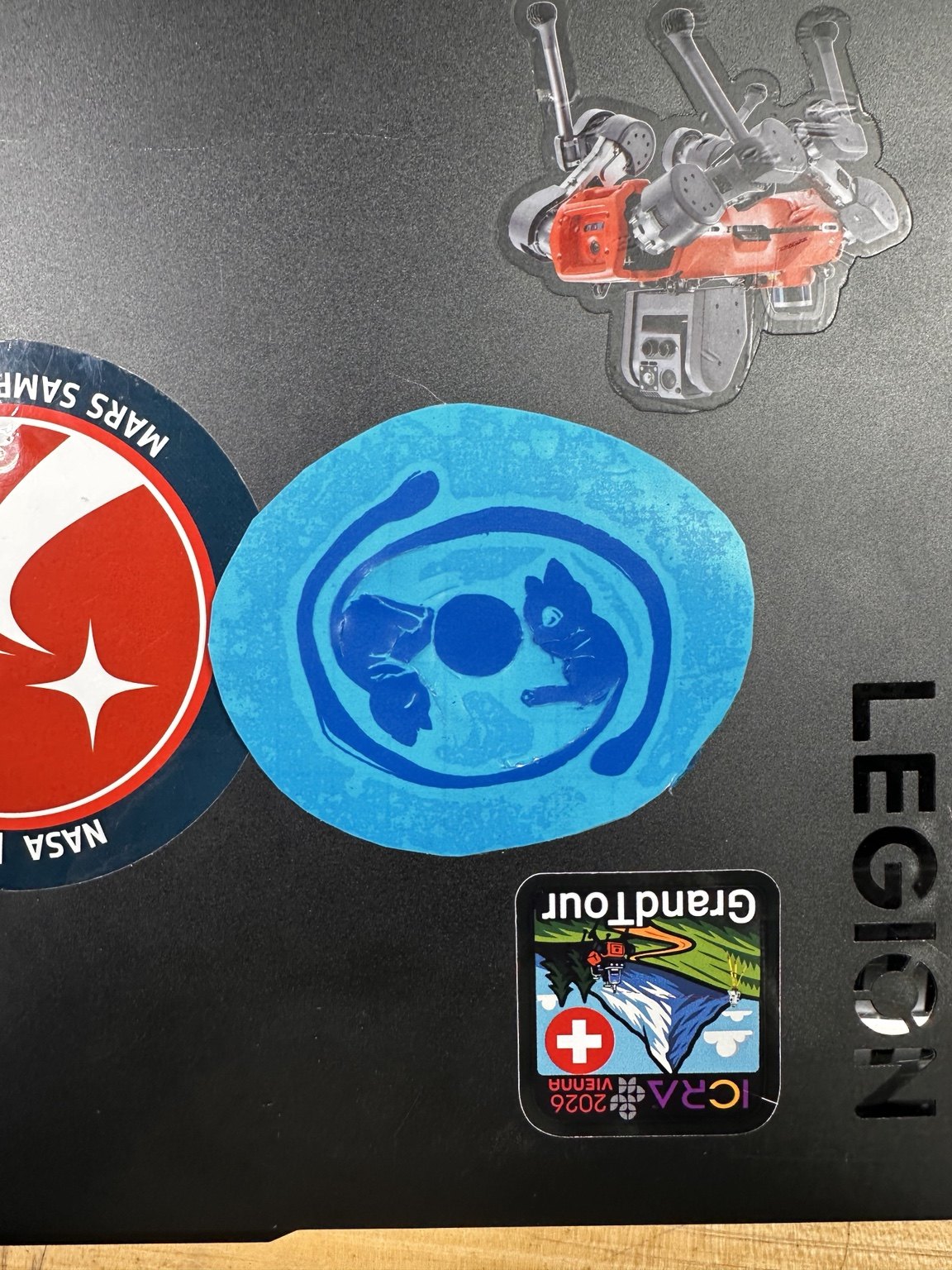 Completed two-tone blue vinyl sticker beside NASA and robotics stickers on a laptop