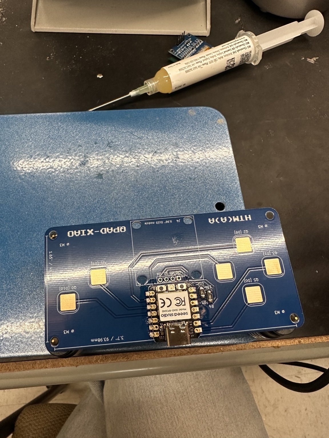 Seeed XIAO RP2040 placed on the QPAD PCB on the workbench, with solder-paste syringe nearby