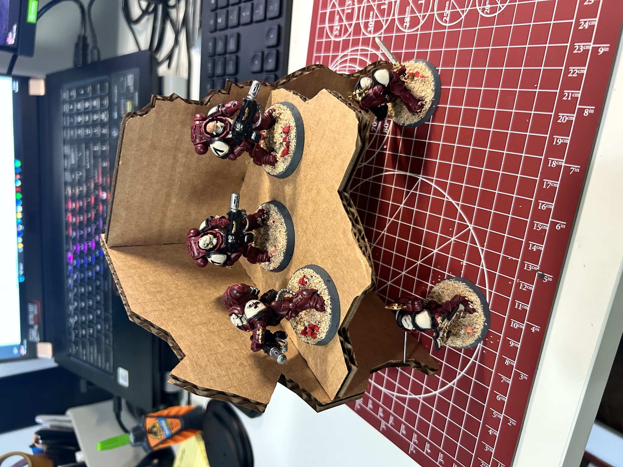 The assembled cardboard terrain piece with five painted Space Marine models on the upper shelf and on the mat around it