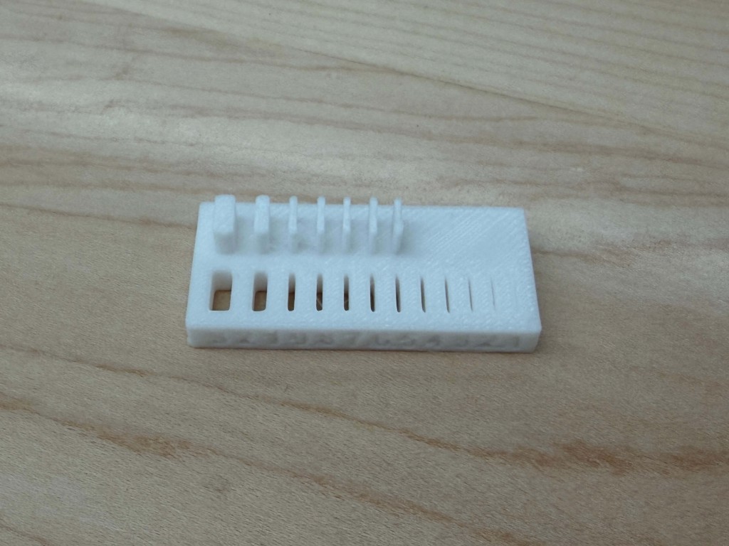 White printed plate with slots, holes, and thin pins of decreasing size
