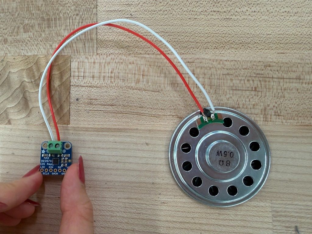 Amplifier breakout wired with red and white wires to a round speaker on a wood table
