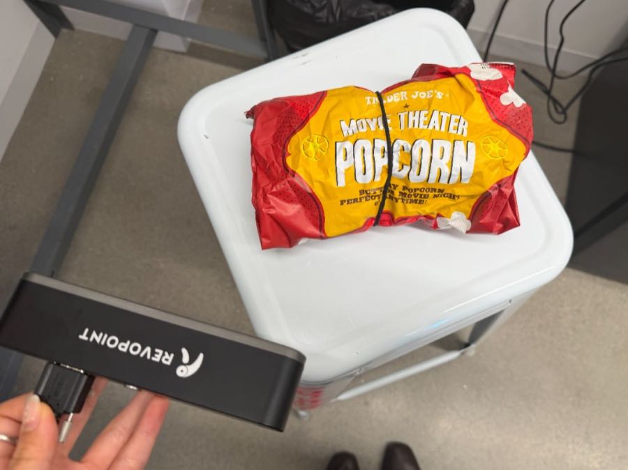 Hand holding a Revopoint scanner in front of a bag of Trader Joe's popcorn