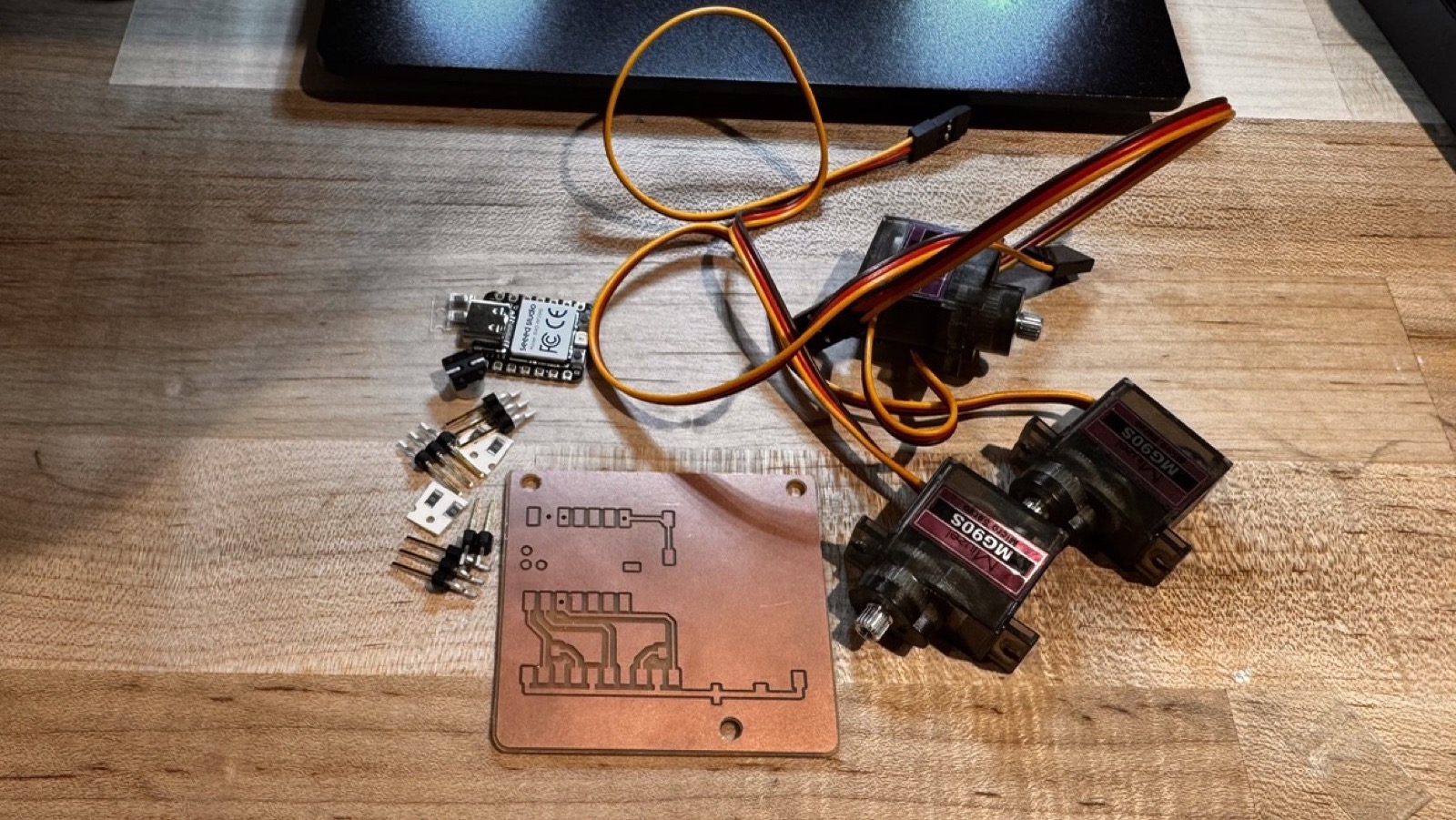 The milled version 1 board on a table with three MG90S servos, pin headers and an XIAO RP2040 ready to be soldered
