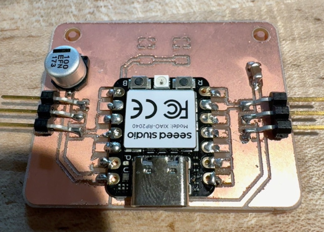 Version 2 board with the XIAO, the 100 microfarad capacitor and two pin headers soldered on, with two empty switch pads at the top
