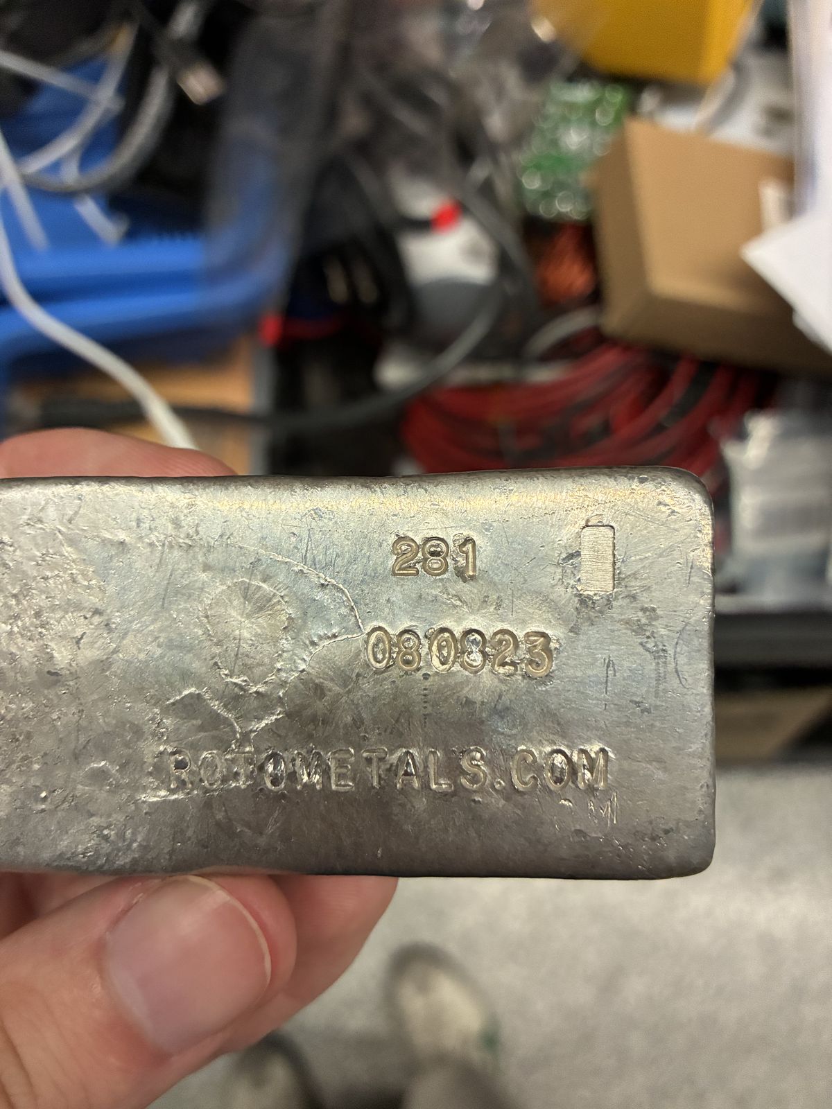 A bar of casting metal stamped ROTOMETALS.COM, held in Victor's hand