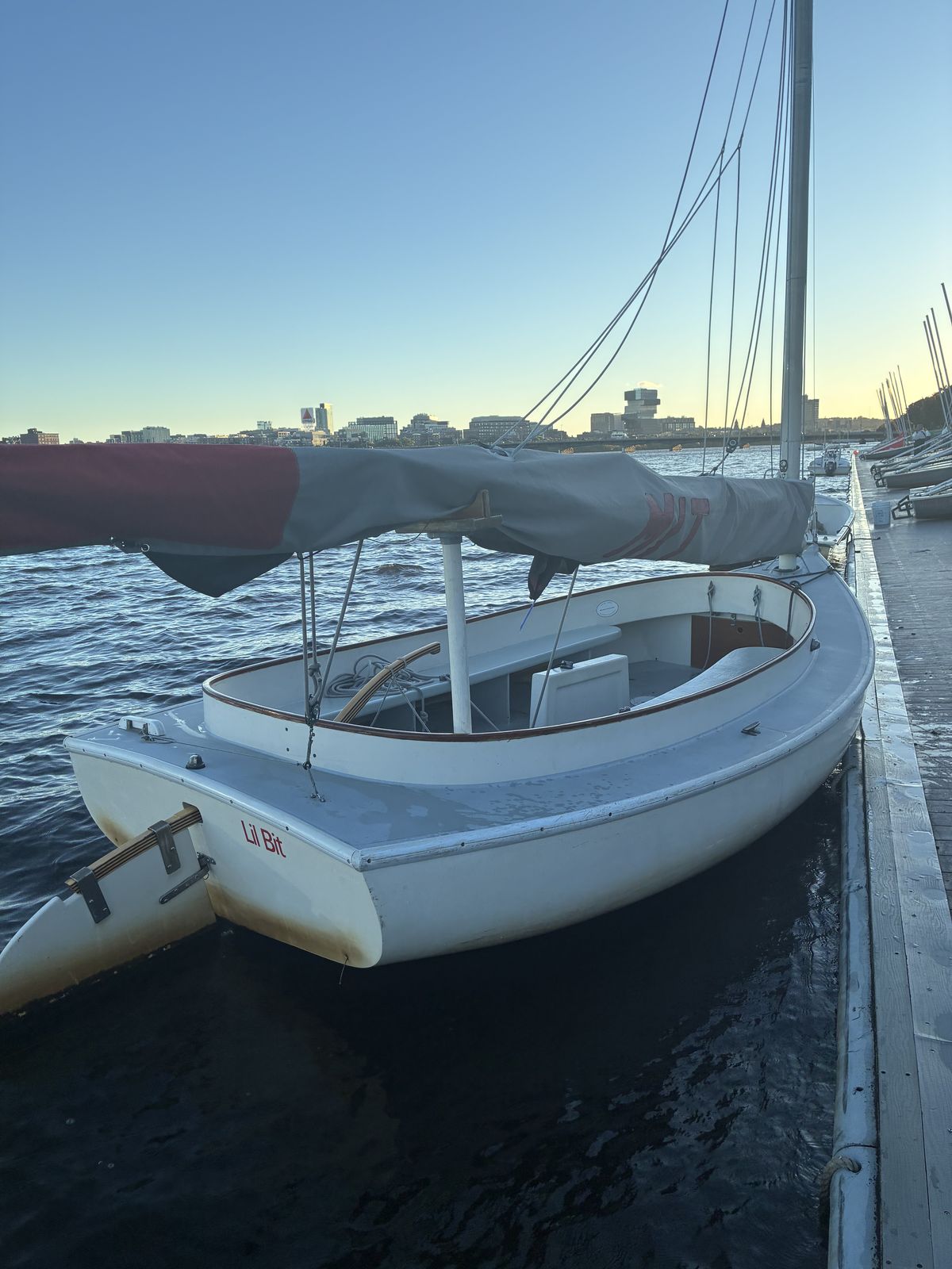 Stern view of the catboat Lil Bit at the dock, showing the wide open cockpit, the wooden tiller and the rudder hanging off the transom