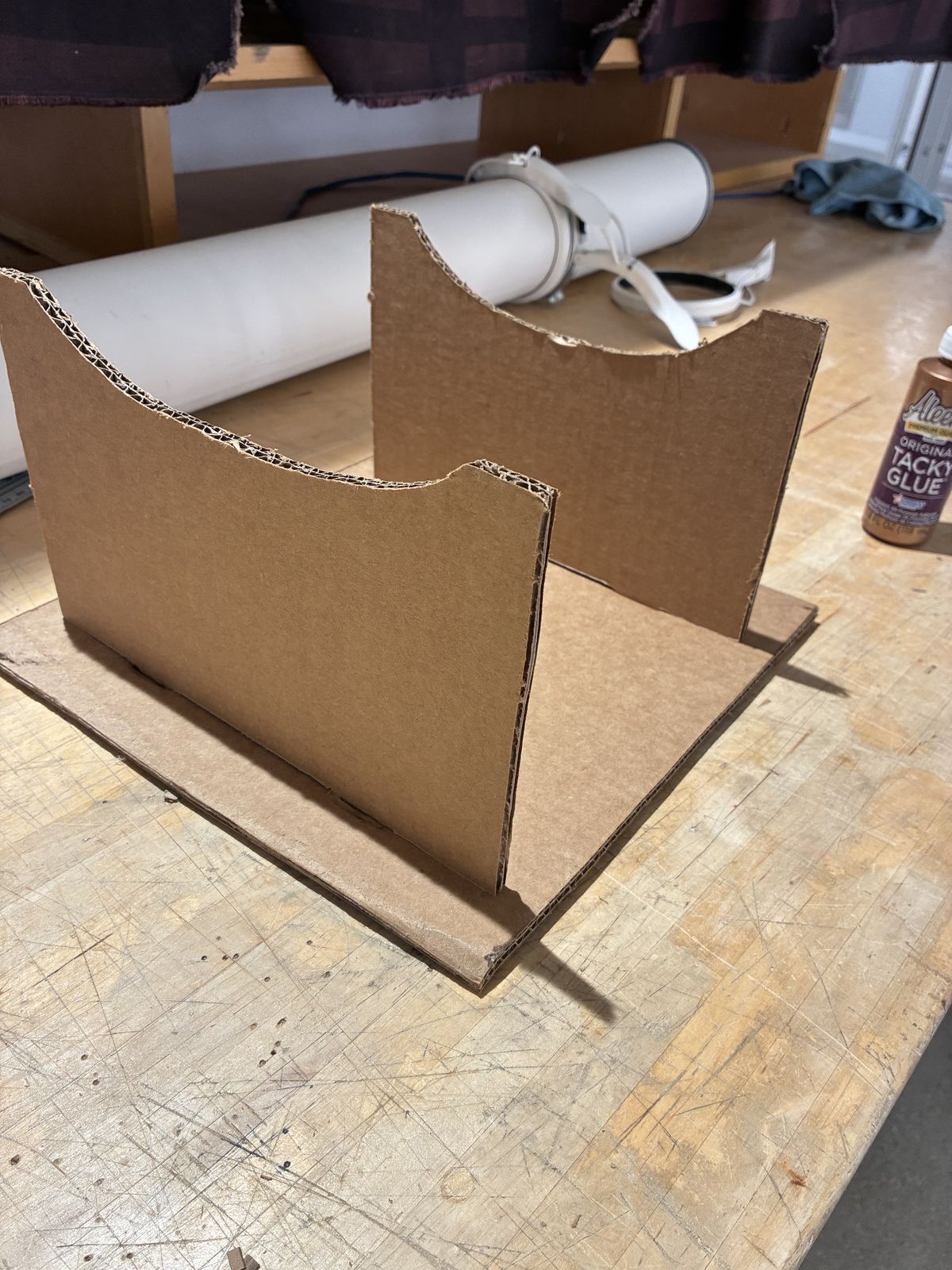 The finished cardboard holder on a workbench: a flat rectangular base with two upright supports facing each other, each with a curved top edge to cradle the hull