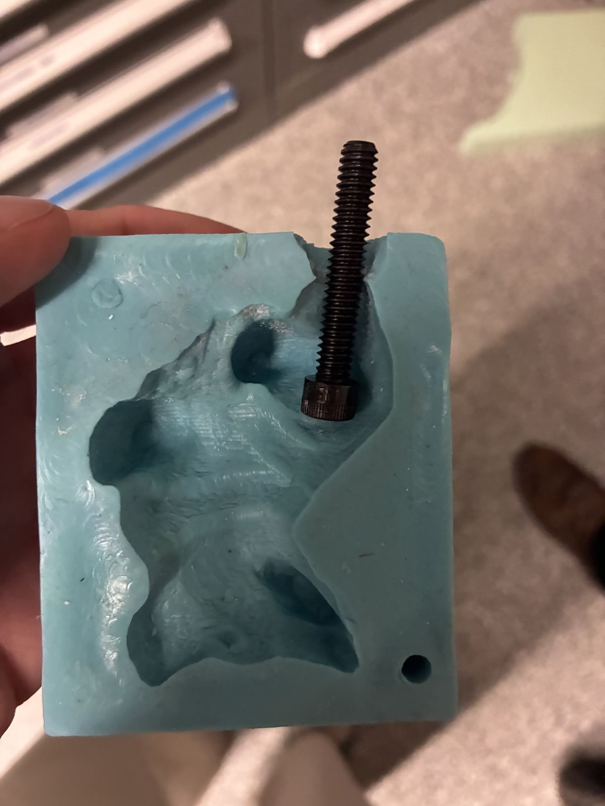 A blue silicone mold held in Victor's hand, with a black screw set into the cavity and sticking out of the top