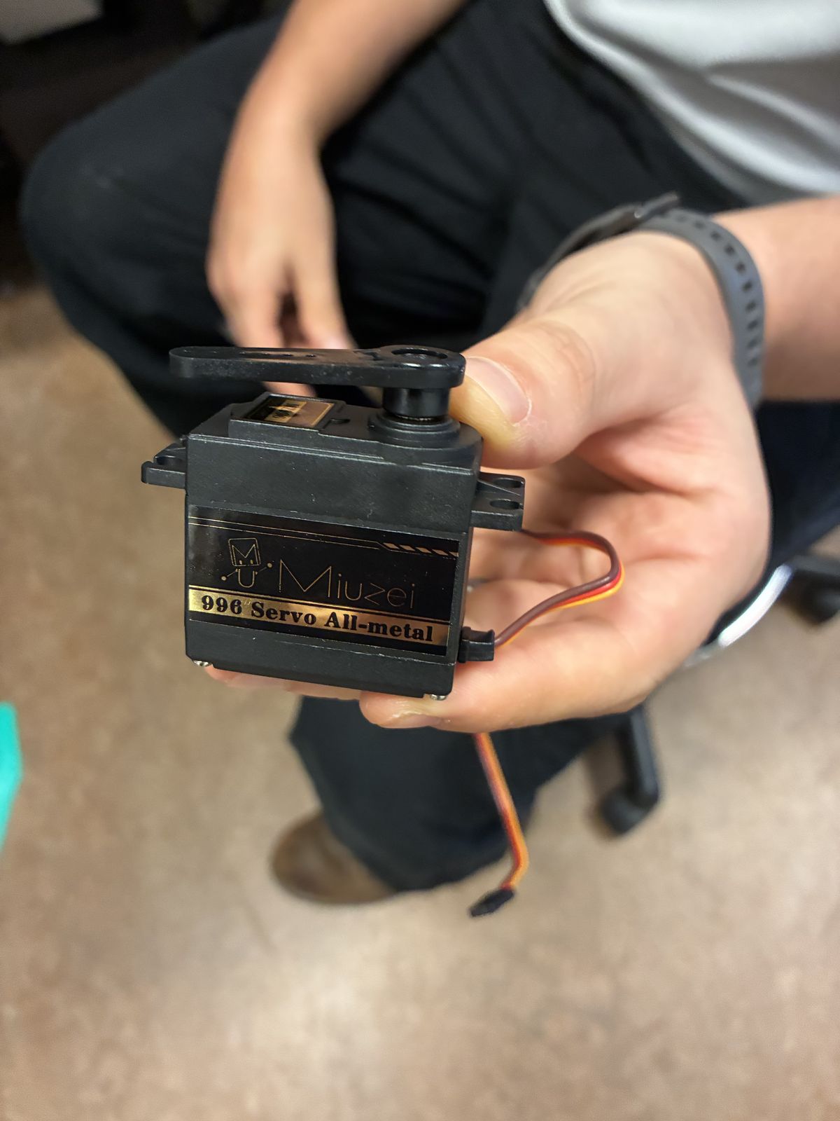 A black Miuzei 996 all-metal servo with a black horn on top and its three-wire cable, held in a hand