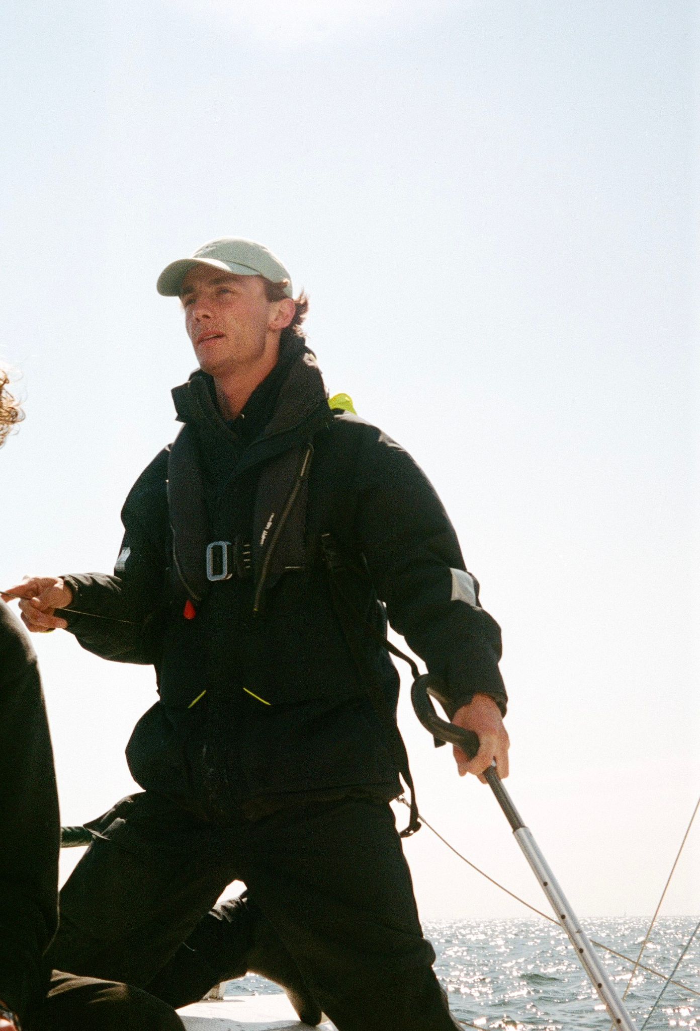 Victor at the helm of a sailboat, wearing a life vest and a cap