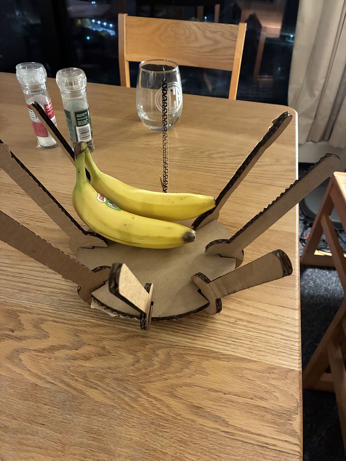 The assembled cardboard fruit bowl on a wooden table, eight branches splaying outwards from the central disc, holding two bananas