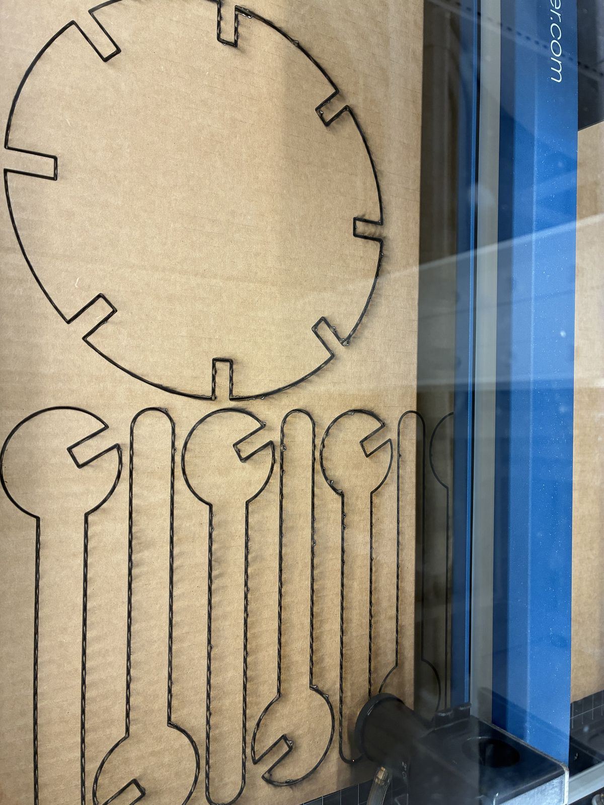 Sheet of corrugated cardboard inside the laser cutter with the disc and several branches cut out, the cut edges burned dark brown