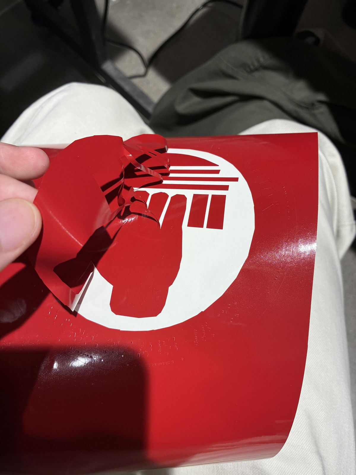 Victor peeling the red vinyl away from its white backing sheet, revealing the white background around the red fist and columns of the logo