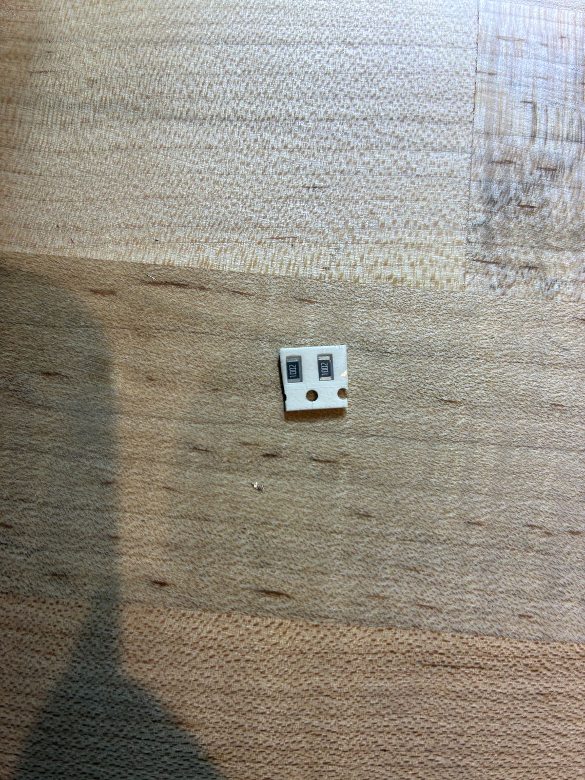 Two tiny surface-mount resistors on a strip of tape on a wooden bench, each printed with the code 1002