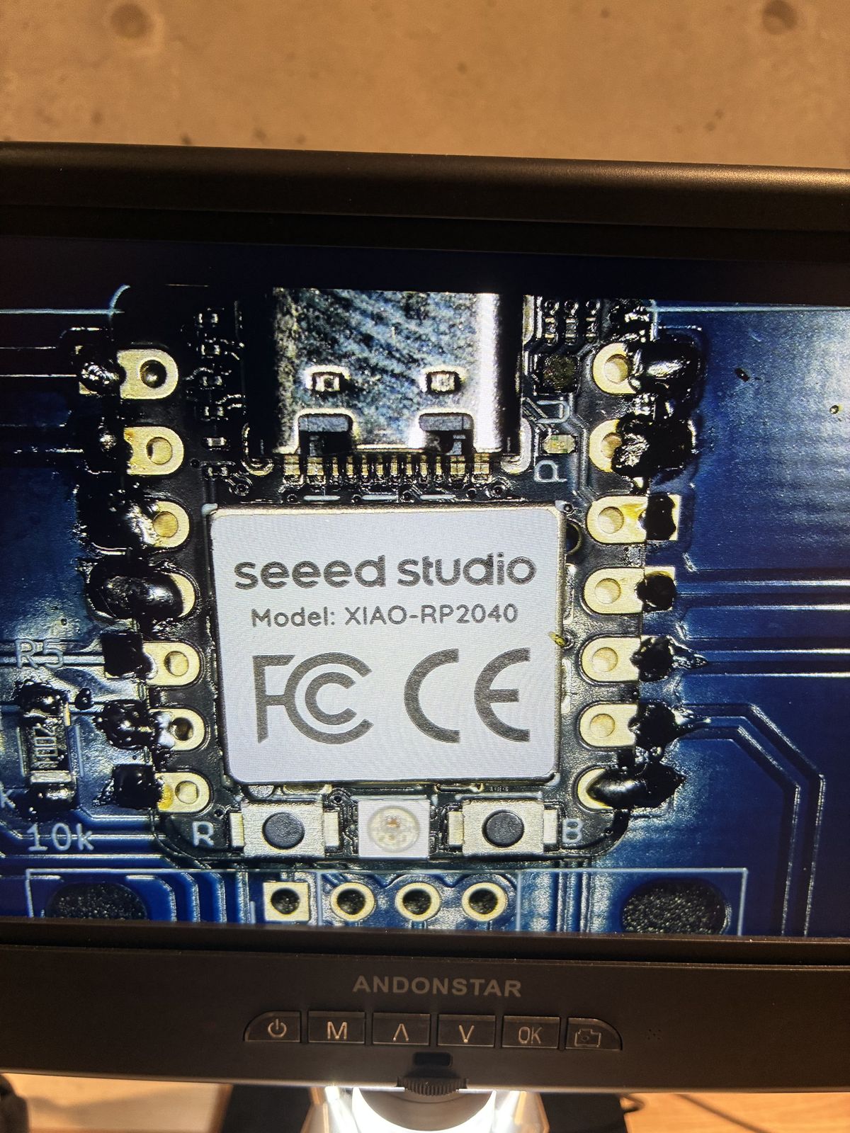 Microscope view of the soldered XIAO module, with large lumpy dark solder blobs covering both rows of pads