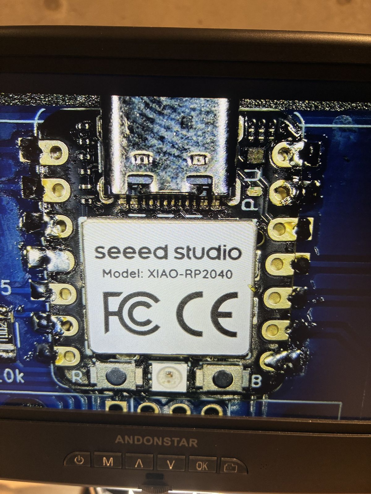 Microscope view of the same XIAO module after rework, the left row of pads more clearly separated but the right row still carrying rounded solder blobs