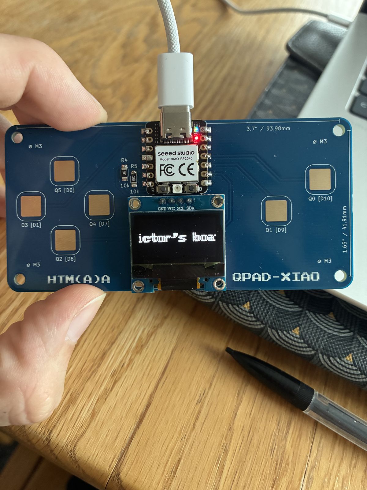 The QPAD-XIAO OLED showing the words Victor's boat part-way through scrolling across the screen, so only the middle letters are visible