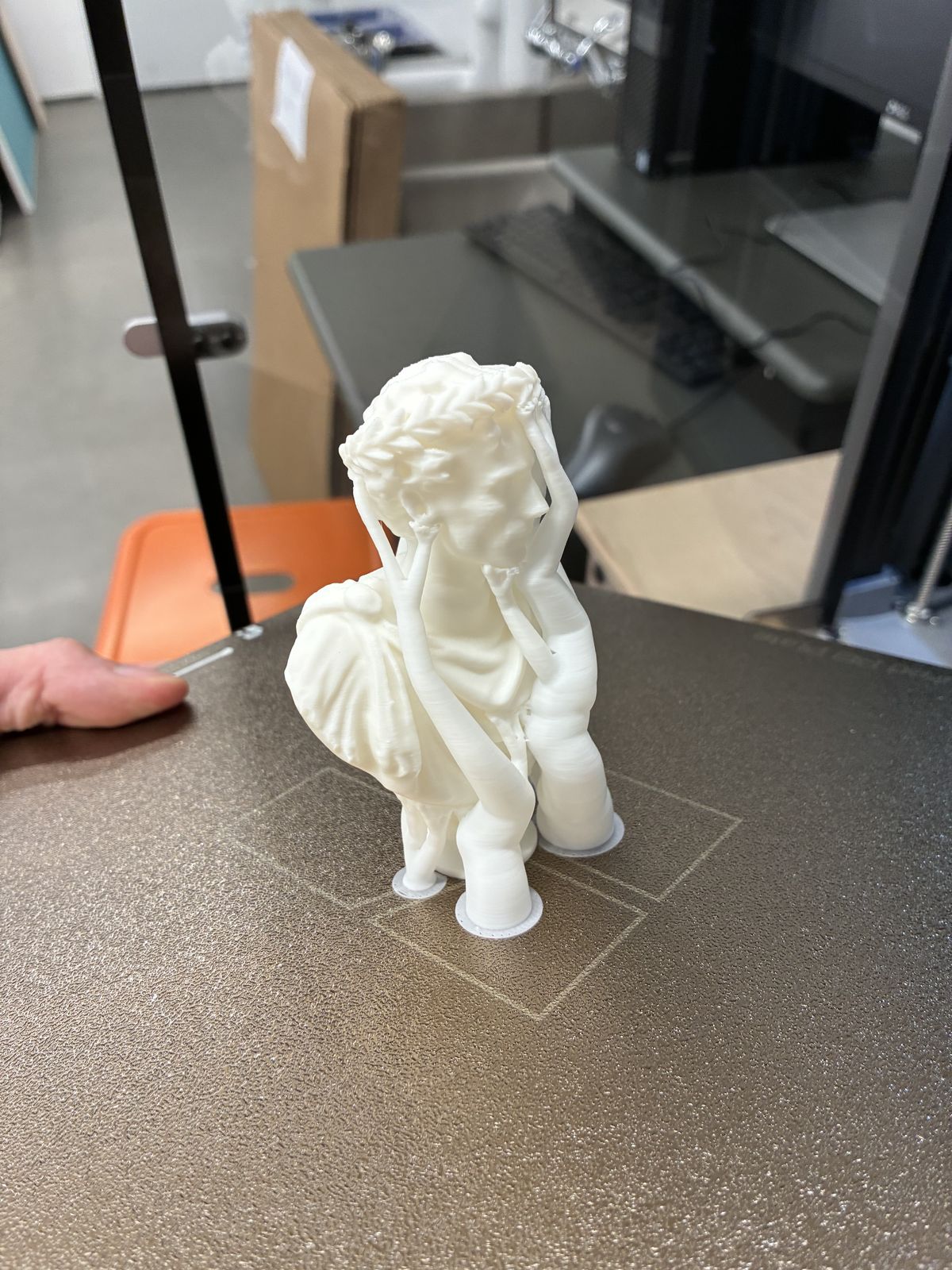 The white printed bust still on the printer bed, surrounded by thin branching tree supports that reach up to hold the face, chin and wreath