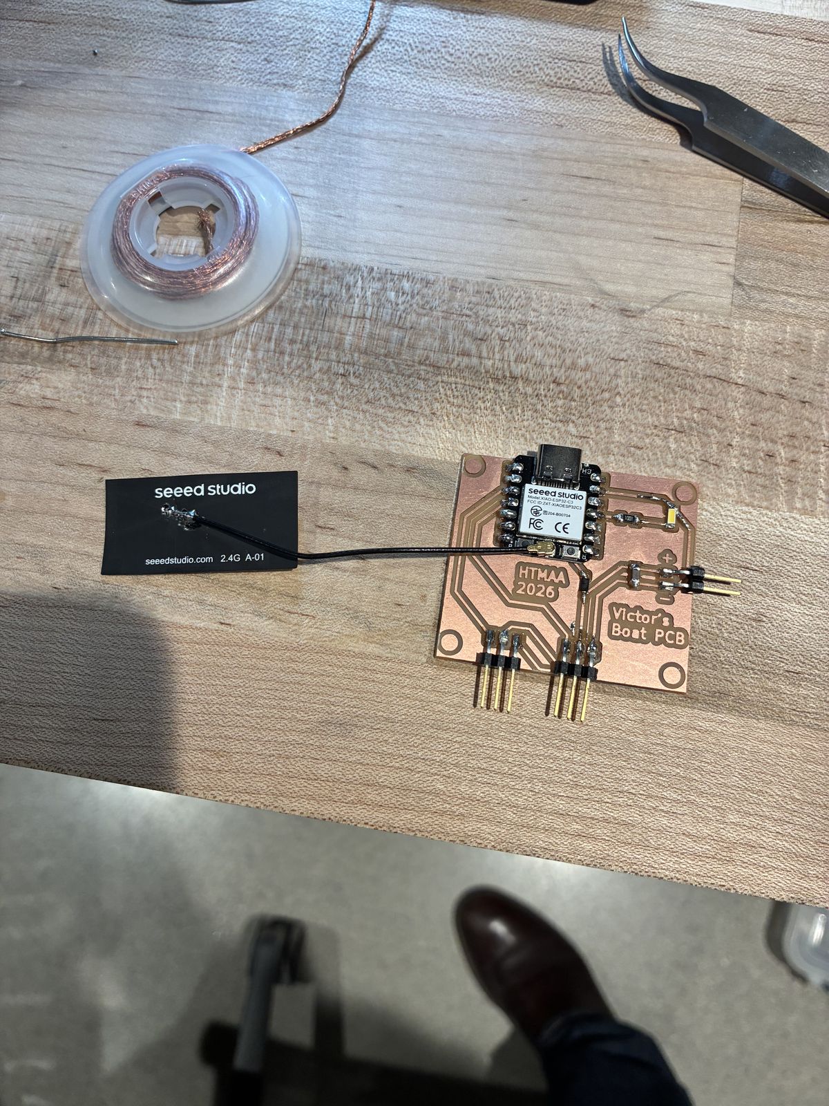 The fully soldered board on the bench, with the XIAO, LED, resistor, diode, capacitor and all three right-angle headers in place, and the Seeed Studio antenna connected to the XIAO