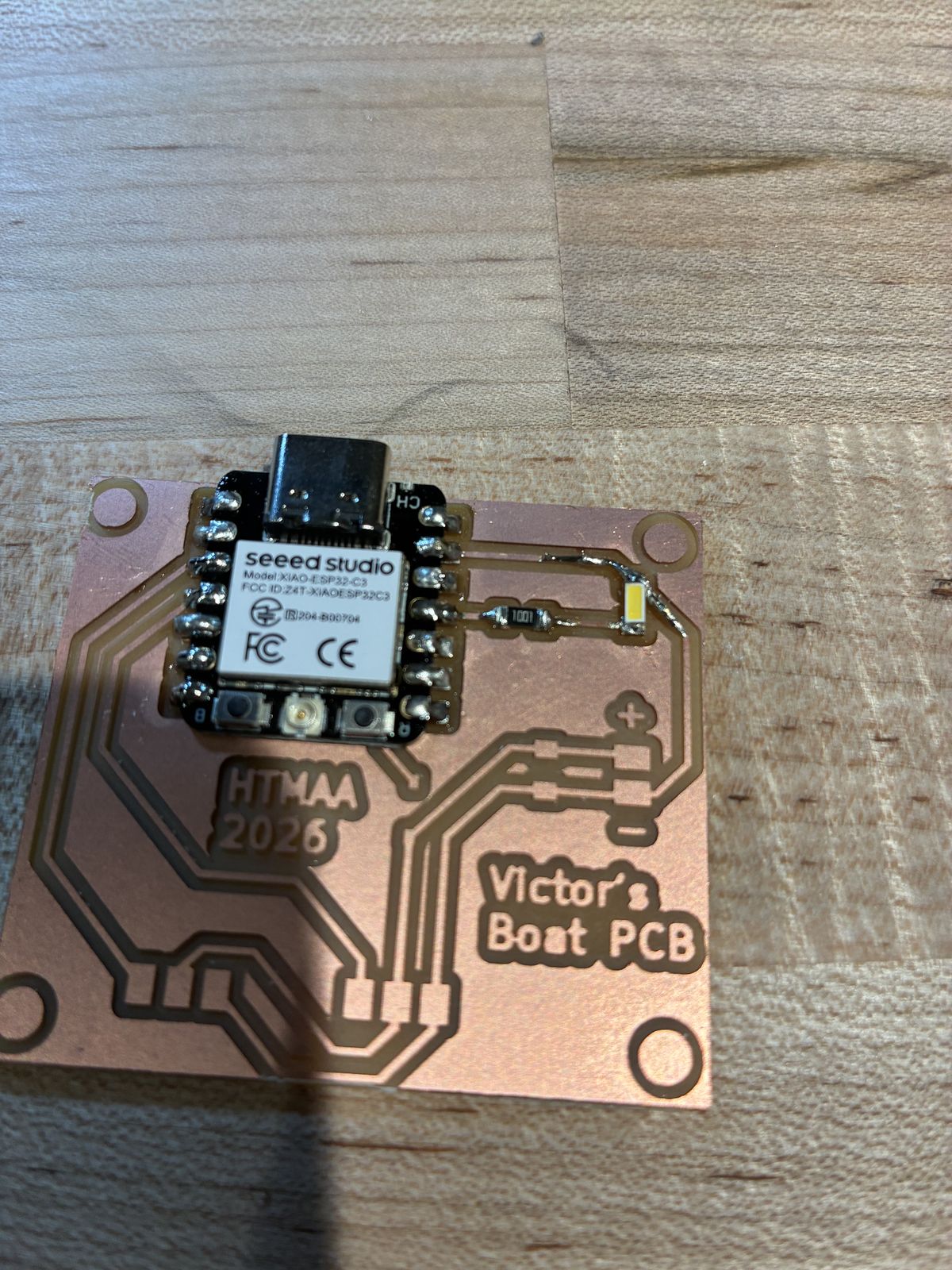 Close-up of the board with the XIAO, the 1001 resistor and the white LED soldered on the right, and a thin bare wire soldered from the XIAO's track to the LED and down along the track, replacing the copper that was torn off