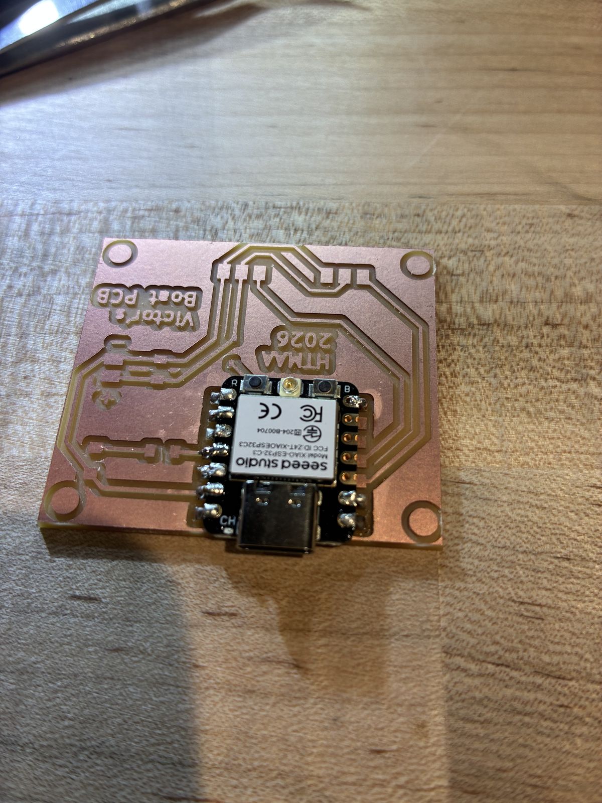 The milled board with the XIAO ESP32-C3 soldered on, seen upside down, with shiny solder joints along both rows of its side pads and the rest of the board still empty