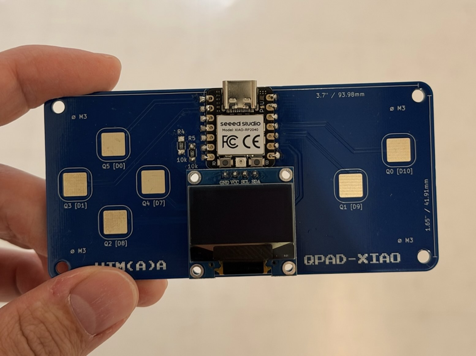 The assembled QPad-XIAO board held upright with its OLED raised above the circuit board