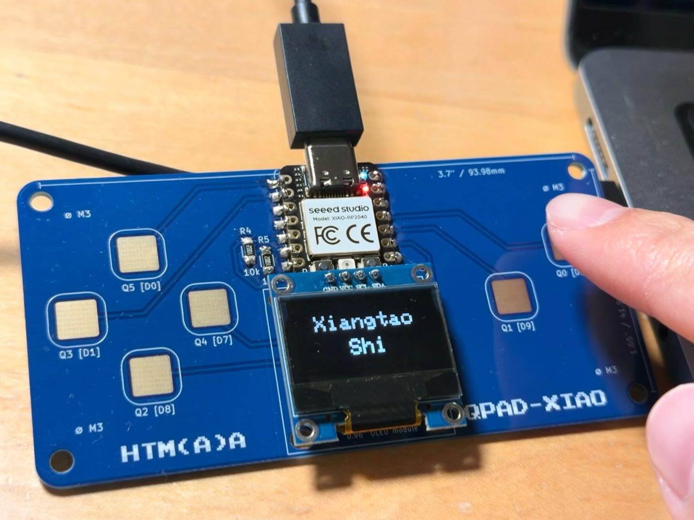 A finger touching Q0 while the OLED displays Xiangtao Shi