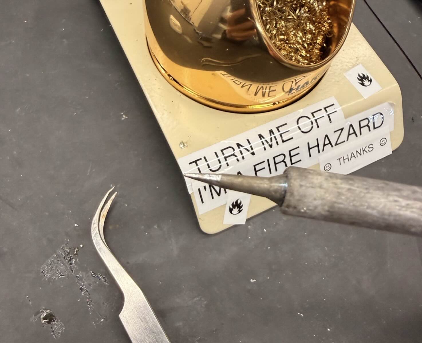 Brass wool tip cleaner, soldering iron, and tweezers on the bench