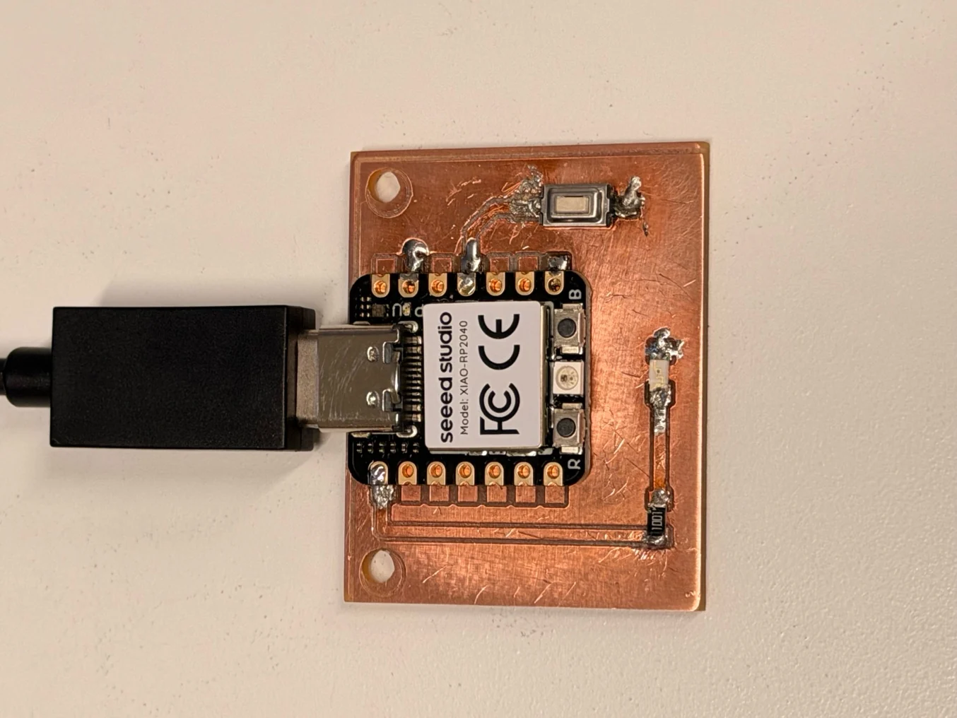 The assembled PCB with a XIAO RP2040, button, resistor and LED connected by USB