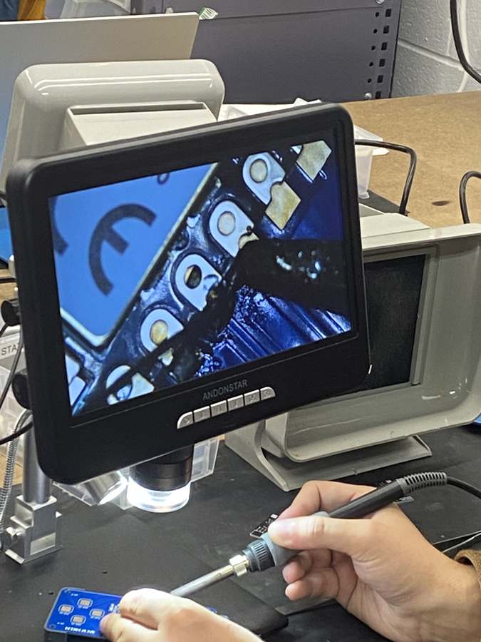 Microscope screen showing Quentin soldering a pin on the board