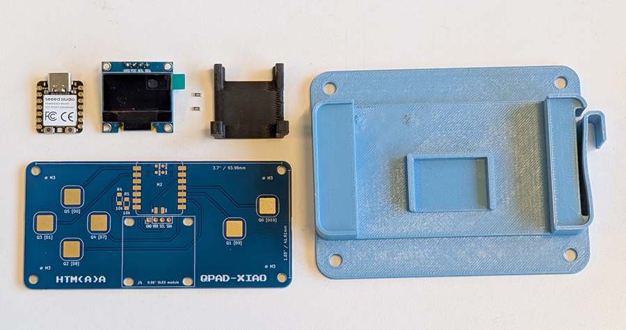 The QPad parts laid out: XIAO RP2040, OLED module, 3D-printed support, blue circuit board and the light blue jig