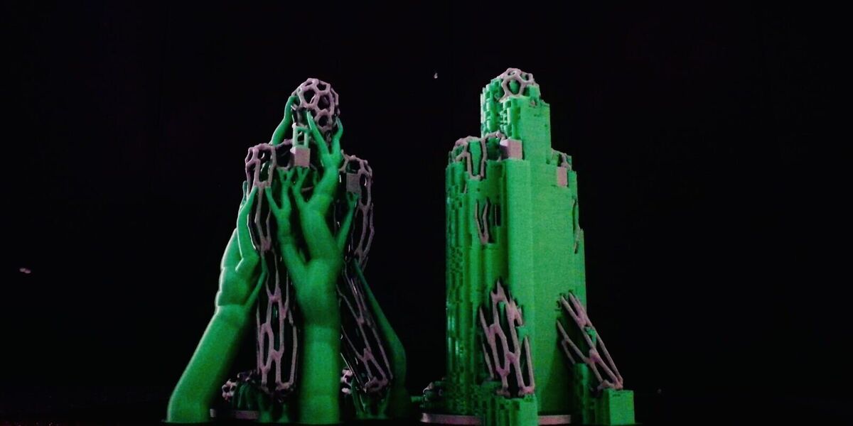 The two figures still wrapped in green supports: tree on the left, normal on the right