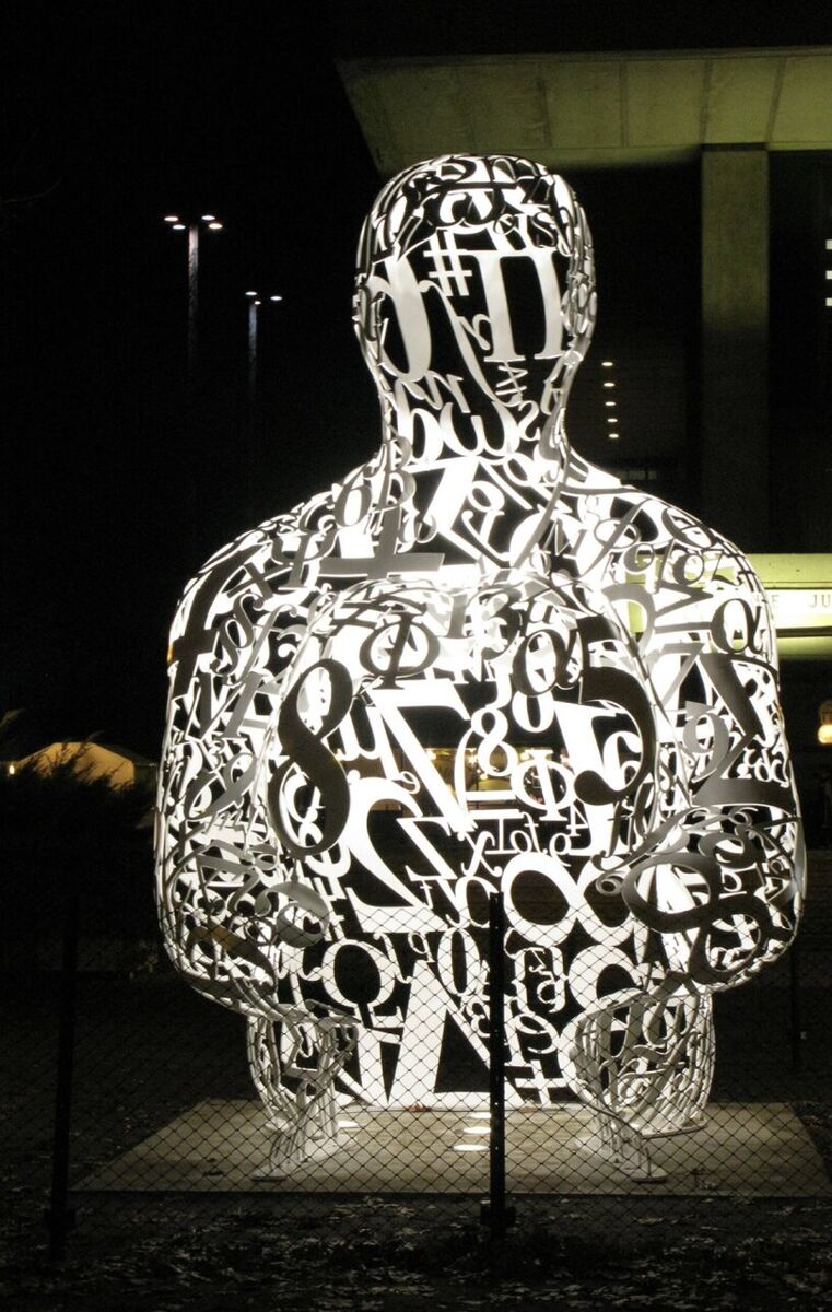 A sculpture of a seated figure made of white numbers and symbols, lit at night
