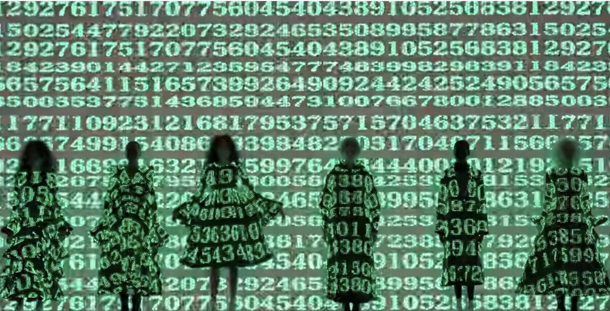 Models in dresses covered in projected green numbers, standing in front of a wall of numbers