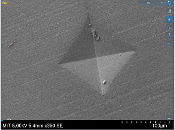 Electron micrograph showing a triangular indentation in a material surface, with a 100 micrometre scale bar